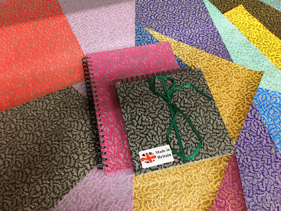 Leaf pattern paper covered Sketchbooks sitting upon assorted coloured papers